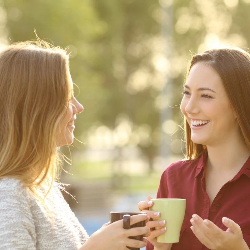 Two women smiling and talking over coffee outdoors